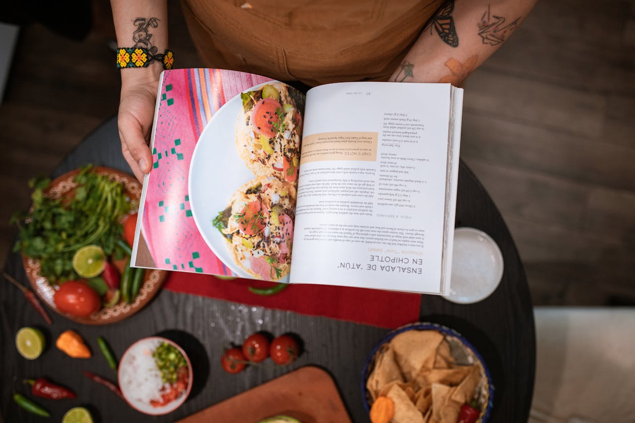 category-02 Close-up of chef holding cookbook over Mexican ingredients on table.