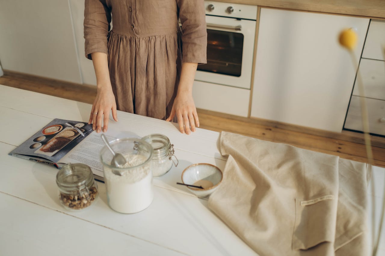 category-01 A person prepares ingredients on a wooden kitchen table with a cookbook for baking.