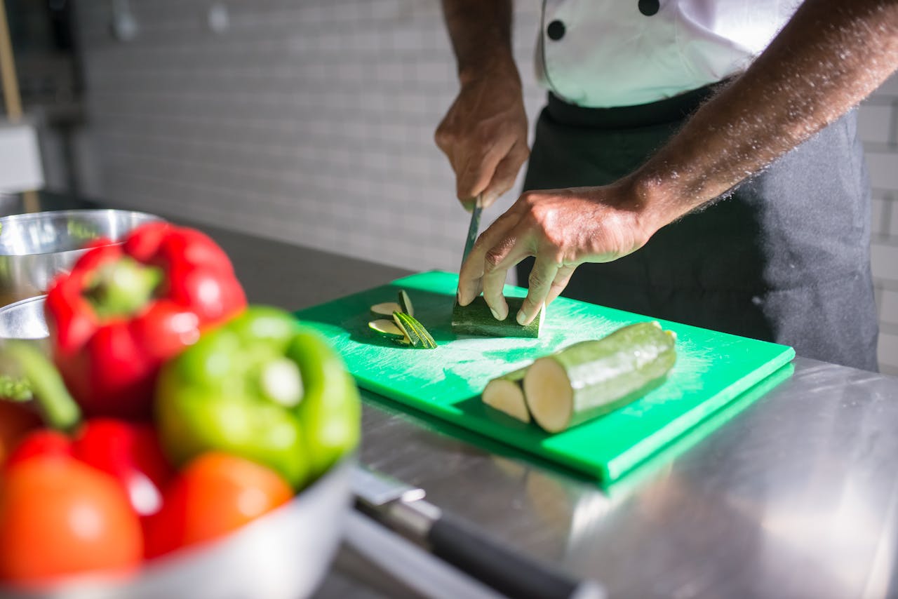 headline Chef slicing zucchini on a green chopping board with fresh vegetables nearby.