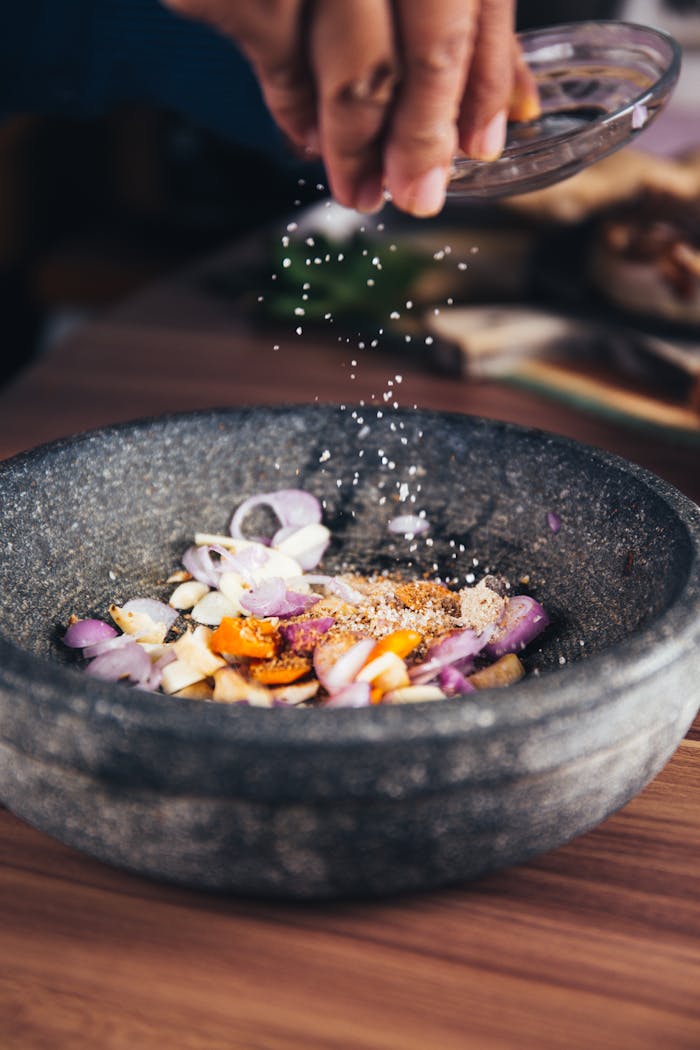 category-05 Close-up of seasoning being added to fresh ingredients in a stone bowl, perfect for culinary themes.